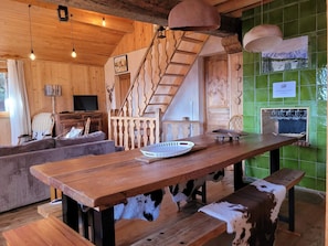A rustic wooden interior with a wooden staircase, a dining table with a cowhide bench, a sofa, and a television in the background.