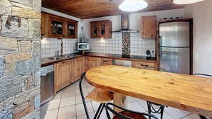 A kitchen with wooden cabinets, a stone wall, a tiled backsplash, and a stainless steel refrigerator. - Cozy 4* chalet near slopes with parking and wifi for 14 guests (Le Corbier)