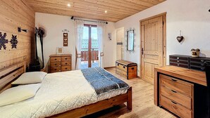 A wooden room with a bed, dresser, and a door leading to a balcony. - Cozy 4* chalet near slopes with parking and wifi for 14 guests (Le Corbier)