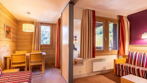 A cozy room with a bed, a sofa, a dining table with chairs, and a window with curtains. - Apartment with balcony, parking, near La Plagne center (La Plagne 1800)