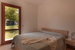 Un dormitorio con cama, mesita de noche, ventana y vista a una casa y jardín.