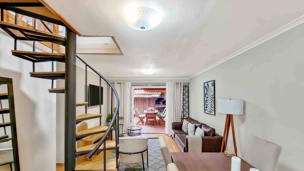 Una sala de estar moderna con una escalera de madera, un comedor con mesa y sillas, y un sofá.