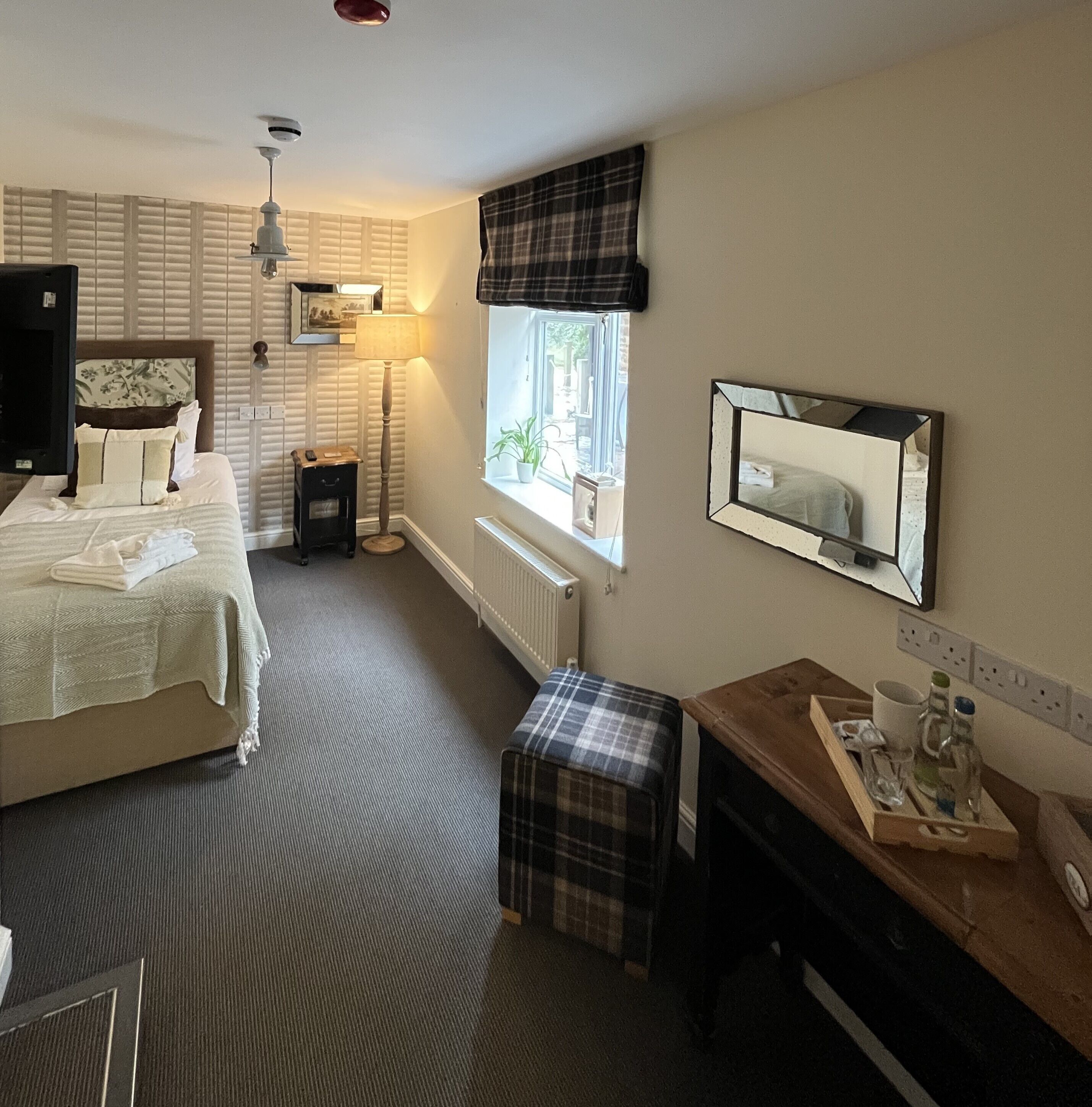 Habitación de hotel con cama, mesita de noche, lámpara, ventana con vistas y escritorio con espejo.