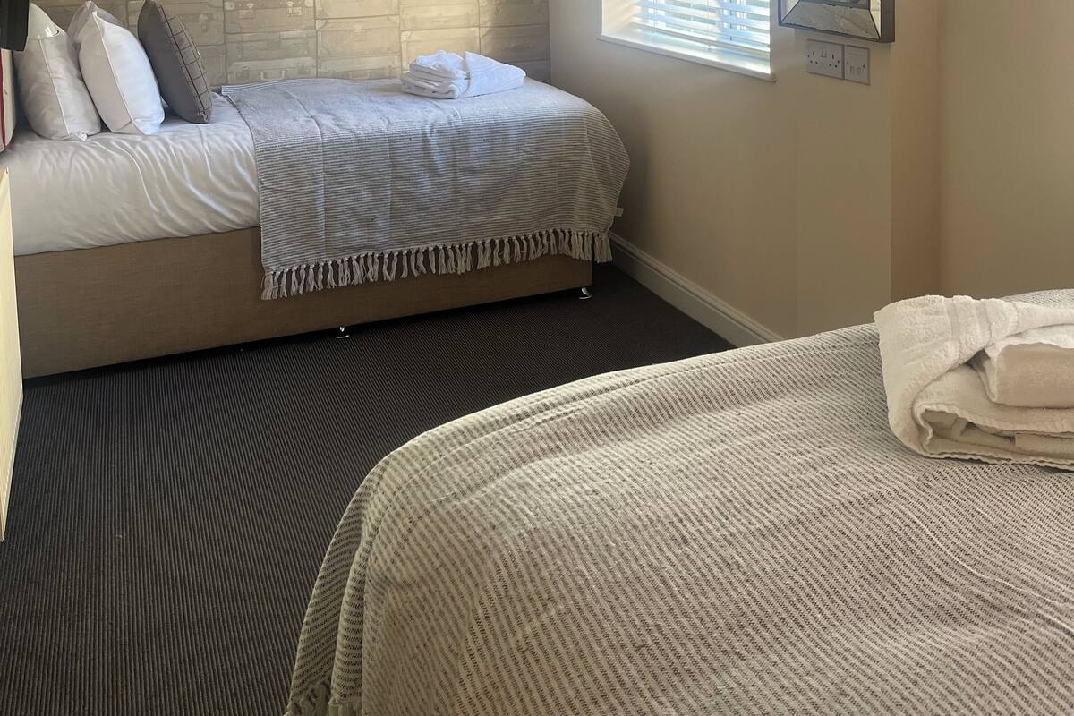 A hotel room with a bed, a window with blinds, a wall-mounted light fixture, and a ceiling fan.