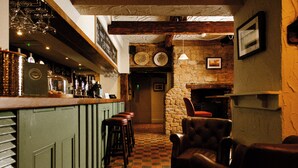 A bar area with stools, a stone wall, and a fireplace. - The Olde Coach House Inn  (Rugby)