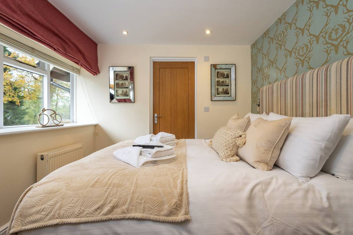 A neatly made bed with a beige blanket and pillows, a wooden door, and framed pictures on the wall.