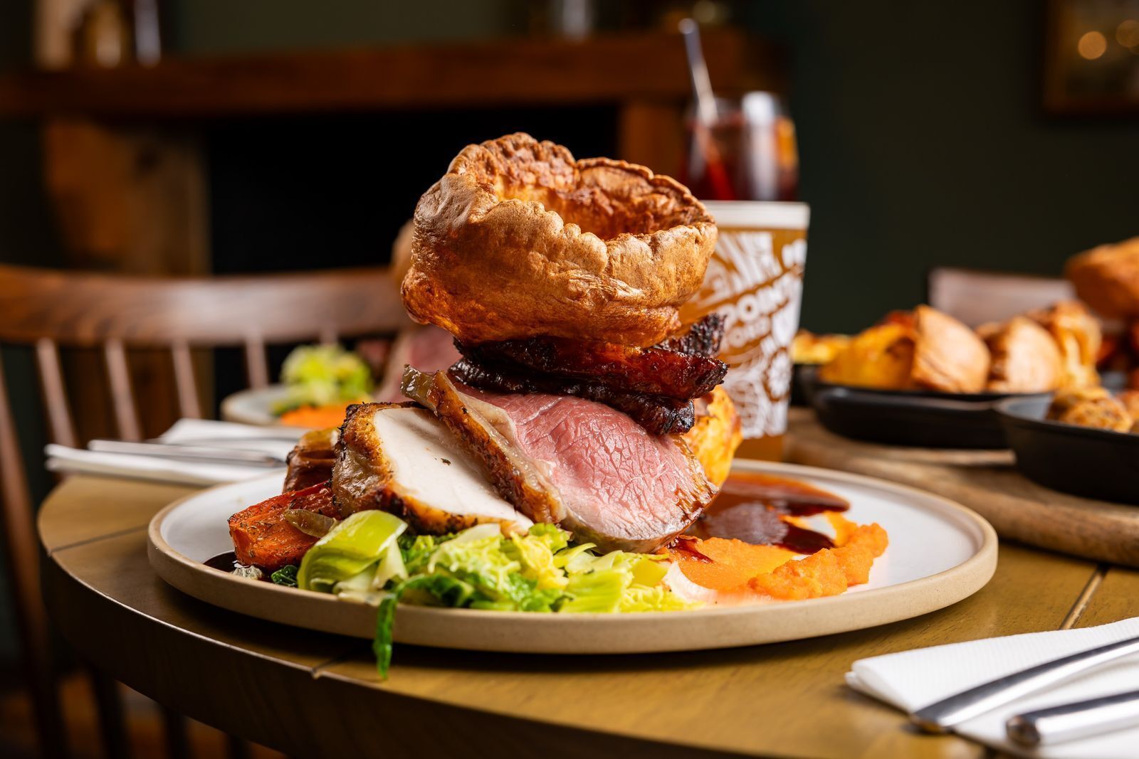 A plate with a pork chop, Yorkshire pudding, and a slice of meat, possibly beef, on a wooden table.