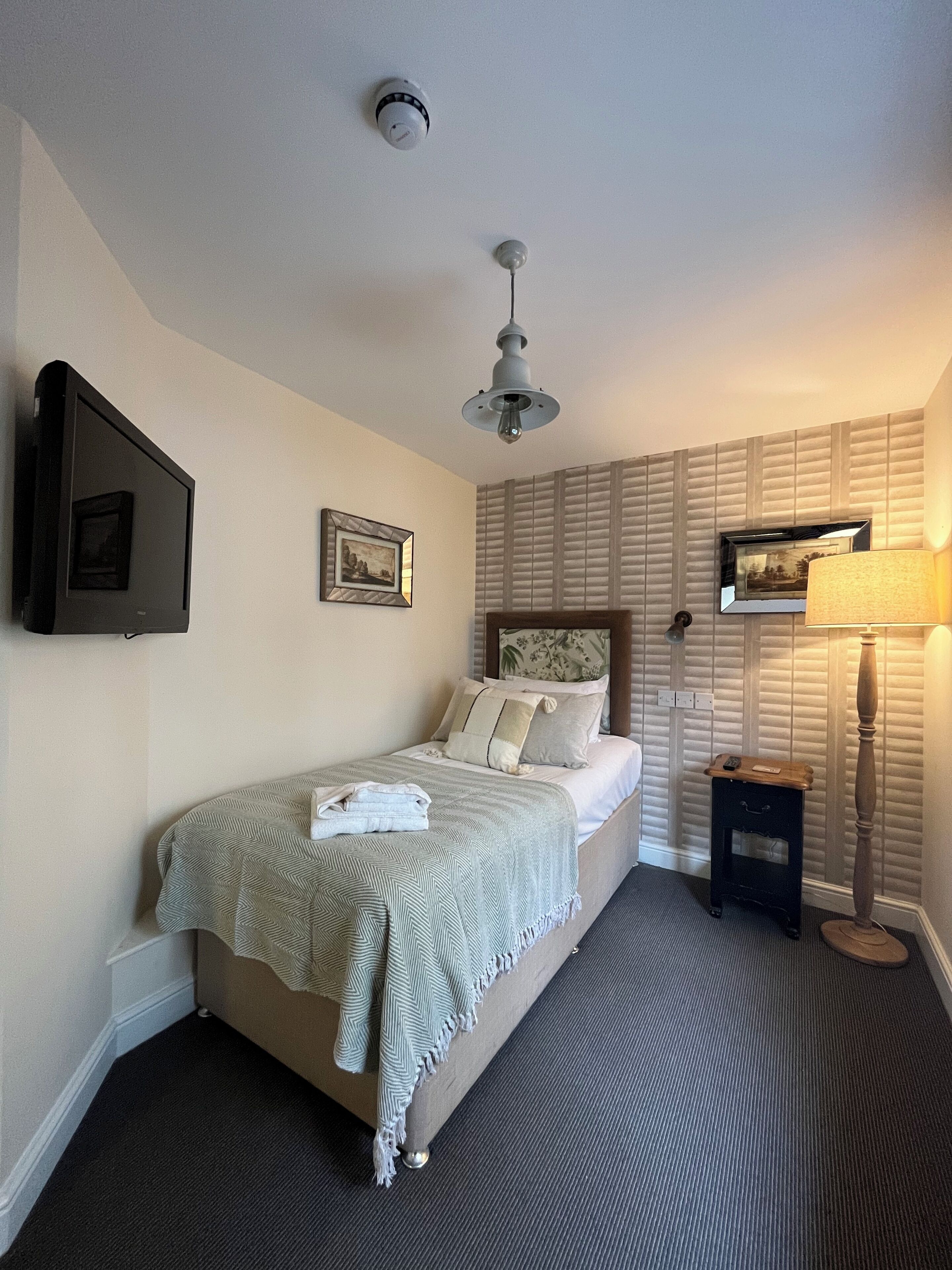 A neatly arranged bedroom with a bed, a television, a ceiling fan, and a bedside table with a lamp.