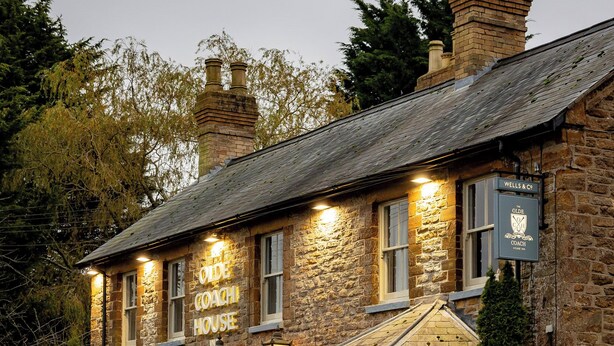 A stone building with a sign reading "The Old Coach House." It features outdoor seating with umbrellas and a wooden fence. - The Olde Coach House Inn  (Rugby)