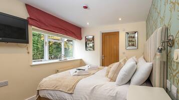 A bedroom with a bed, a TV mounted on the wall, a window with a red valance, and a door.