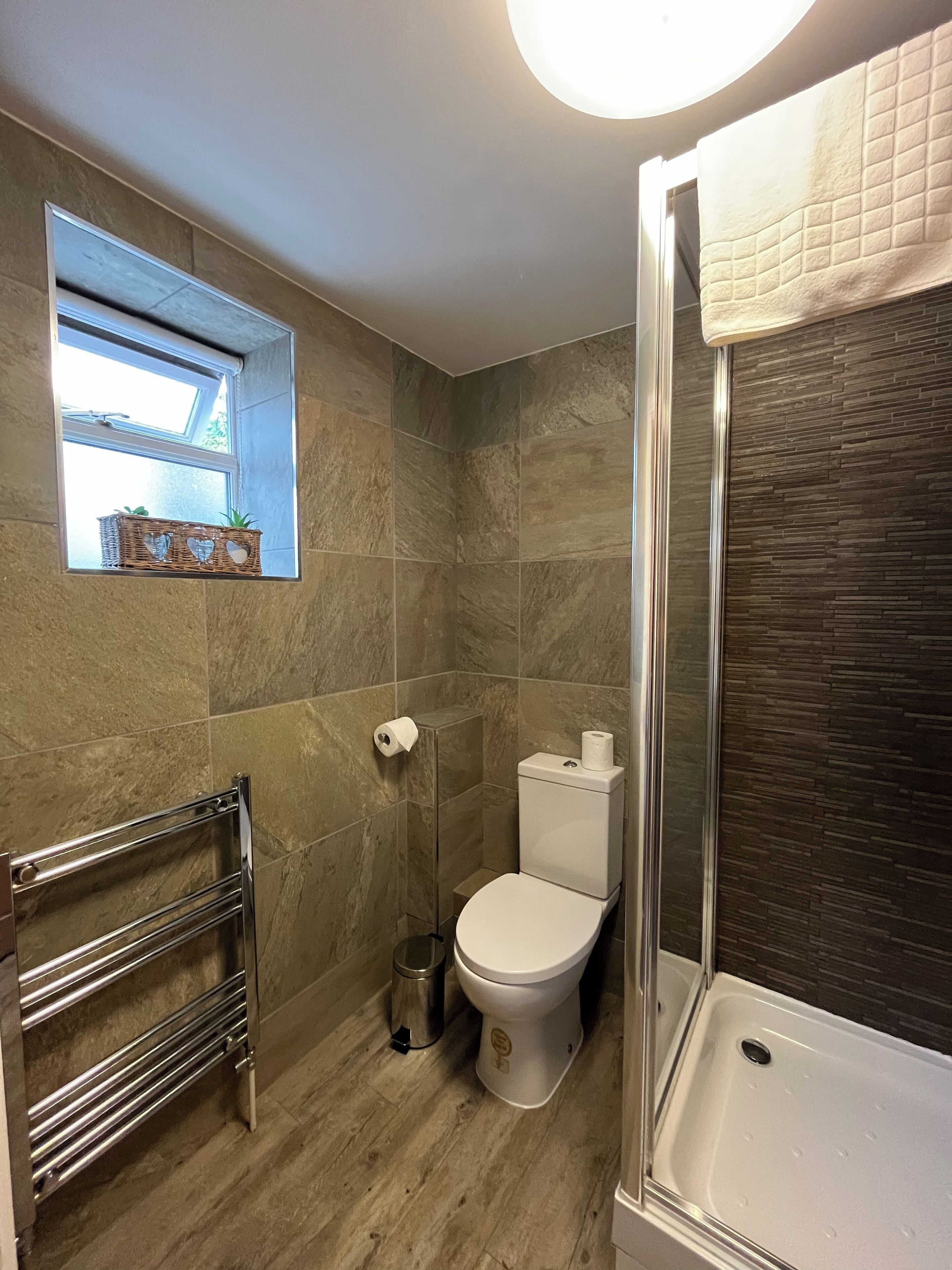 Un baño con ducha, inodoro y una pequeña ventana con una cesta.