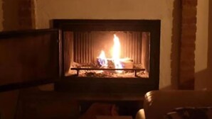 Une cheminée avec un feu qui crépite à l’intérieur, entourée d’un mur de briques et surmontée d’une étagère en bois.