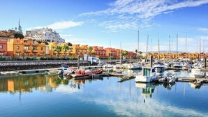 Un puerto deportivo con barcos amarrados, cielo despejado y edificios al fondo.