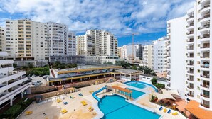 Un hotel con varias piscinas, una zona de playa y vistas de edificios altos circundantes.