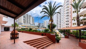 Un espacio al aire libre cubierto con escalones que conducen a una zona de piscina, rodeado de edificios altos y palmeras.