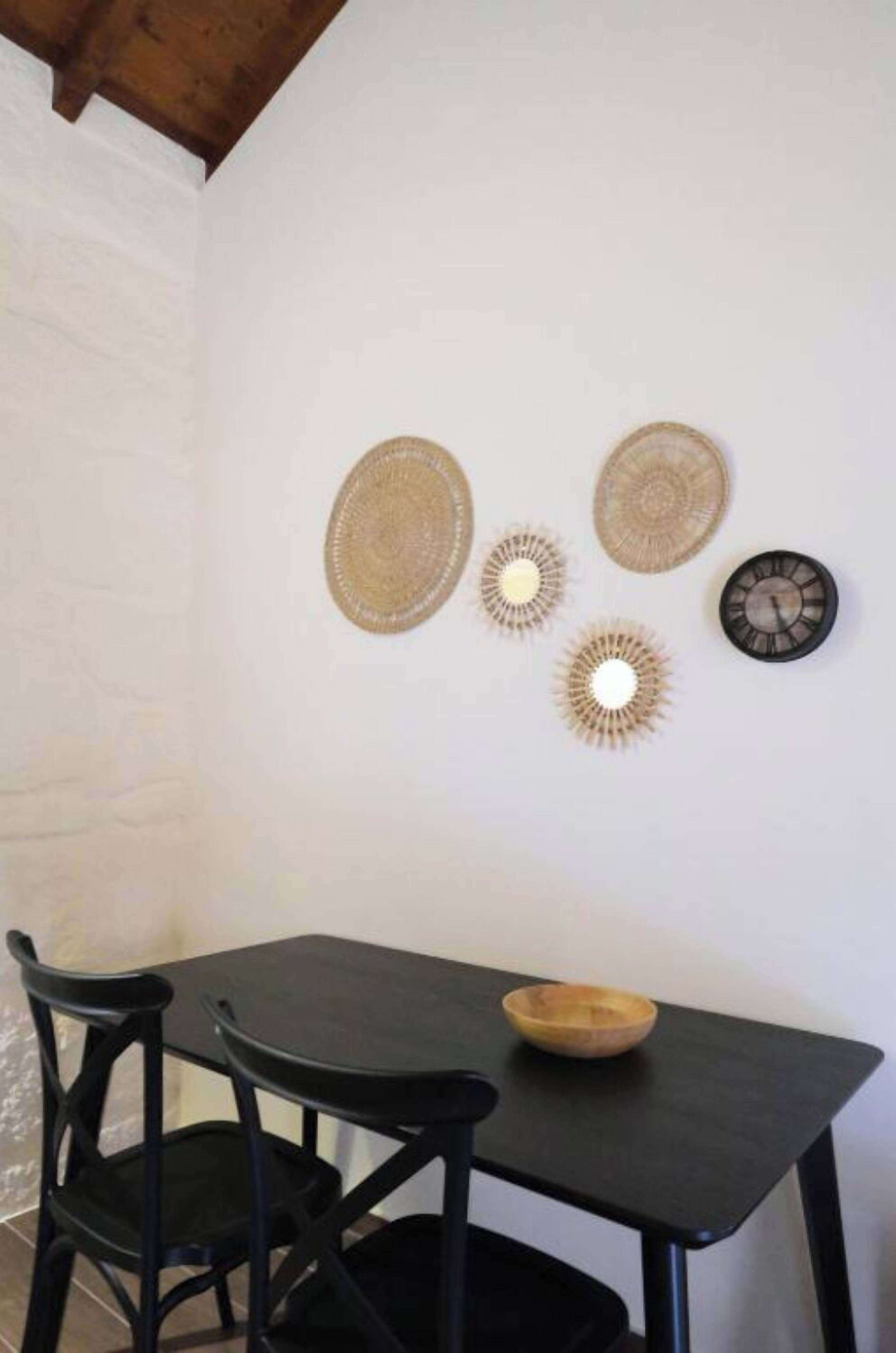 A dining area with a black table and chairs, a wooden bowl on the table, and four wall-mounted decorative items.