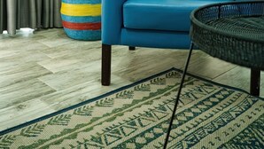Un salon avec un canapé bleu, un tapis à motifs, un pot de fleurs rond en fibres tressées et un mur orn é de trois œuvres d’art circulaires.