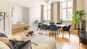 A bright, well-lit room with a bed, a dining table with chairs, a coffee table with snacks, and large windows with curtains. - Tivoli 2 - Spacious 3 Bedroom Near Tivoli (Copenhagen)