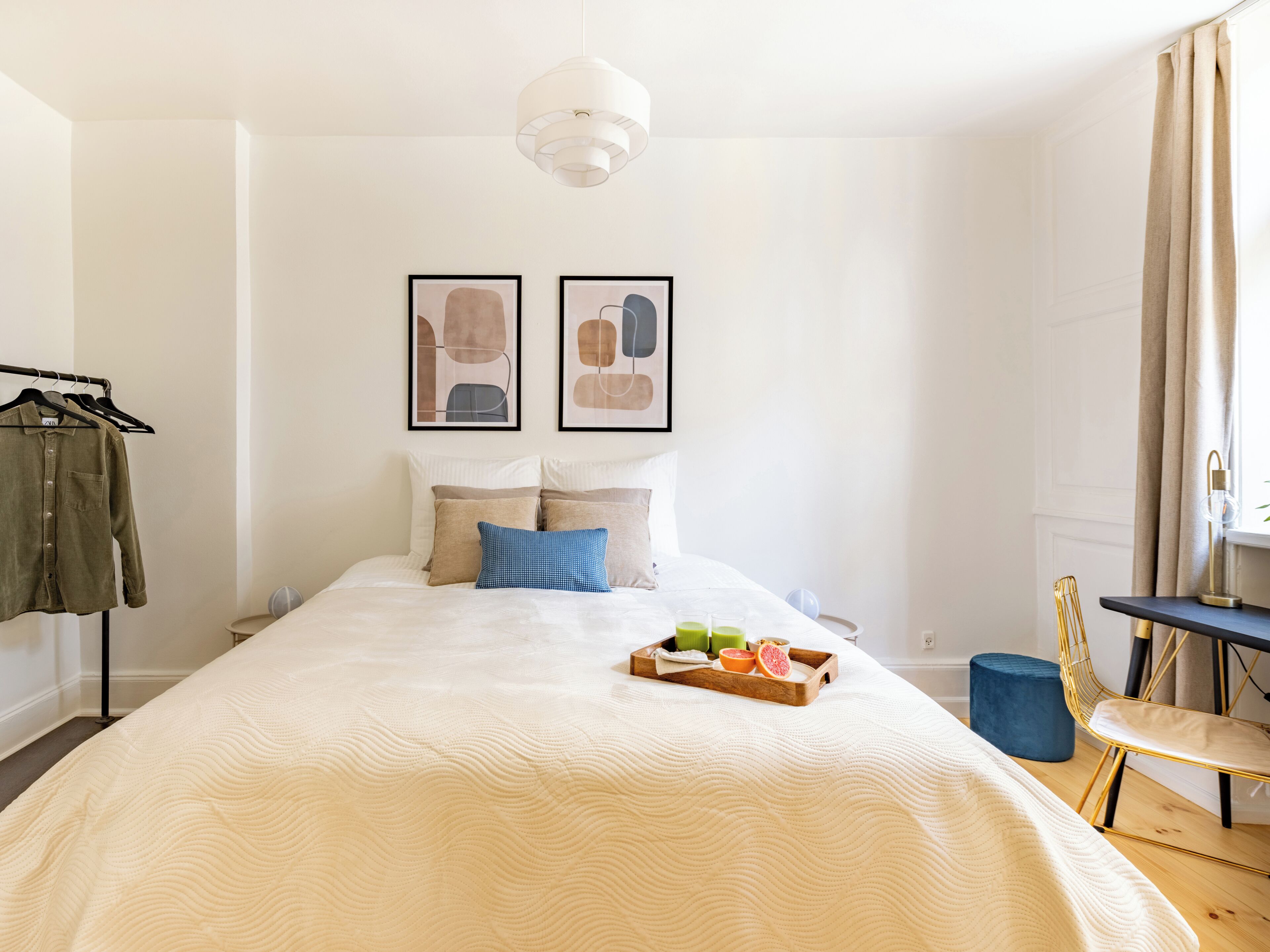 A neatly arranged bedroom with a large bed, a bedside table with a tray of fruit, a chair, and a hanging light fixture.