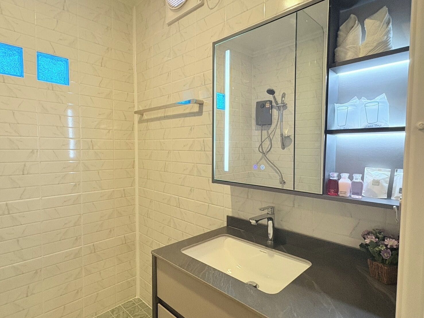 Un baño con lavamanos blanco, un espejo y zona de ducha.