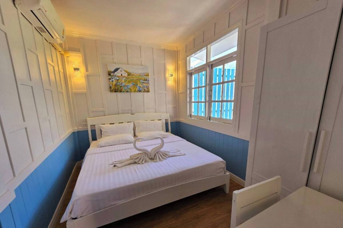Cama arrumada com um arranjo de toalhas em formato de cisne, um quadro na parede e uma janela com persianas.