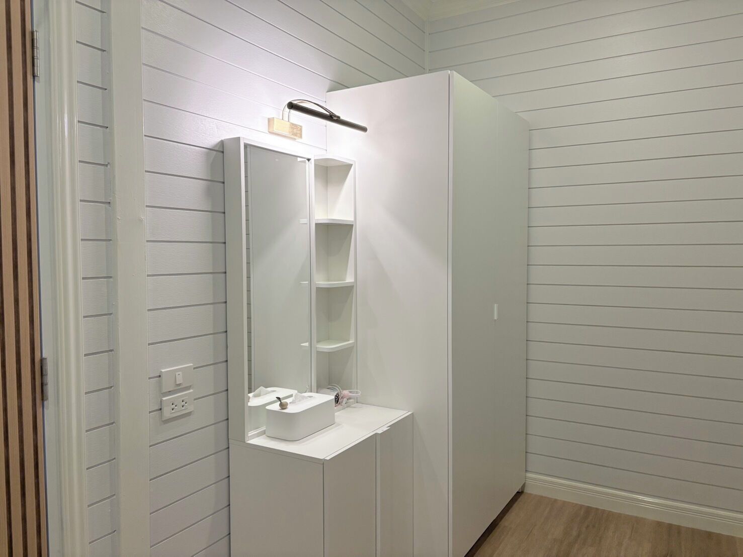 A bathroom with a white vanity, a mirror, and a shelf unit.