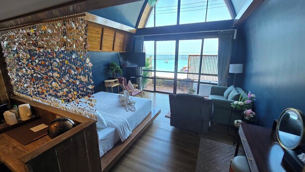 Une chambre à coucher avec un lit, une commode en bois, une grande fenêtre donnant sur la mer et un mur décoré de coquillages.