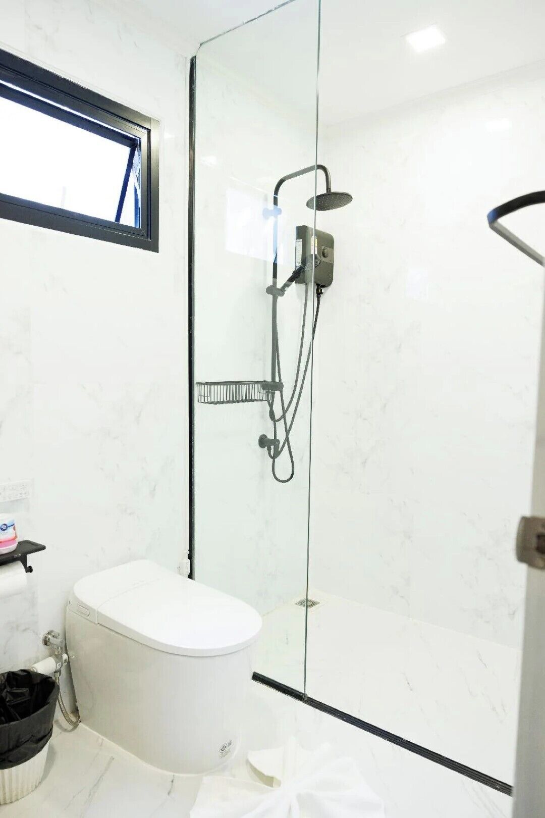 A modern bathroom with a glass-enclosed shower, a white toilet, and a small trash bin.