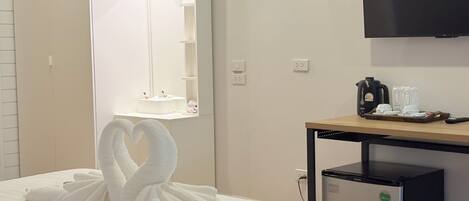 A hotel room with a bed, a bedside table with a coffee maker, a TV, and a mirror with a light above it.