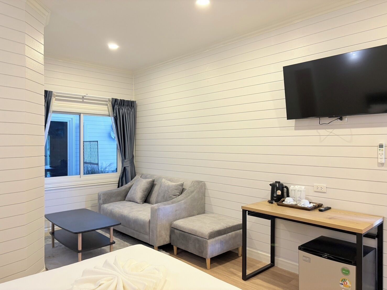 Habitación de hotel compacta con sofá, una mesita, televisor montado en la pared y ventana con cortinas.