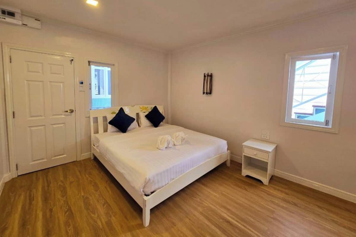 Um quarto com cama, mesa de cabeceira, janela e porta.