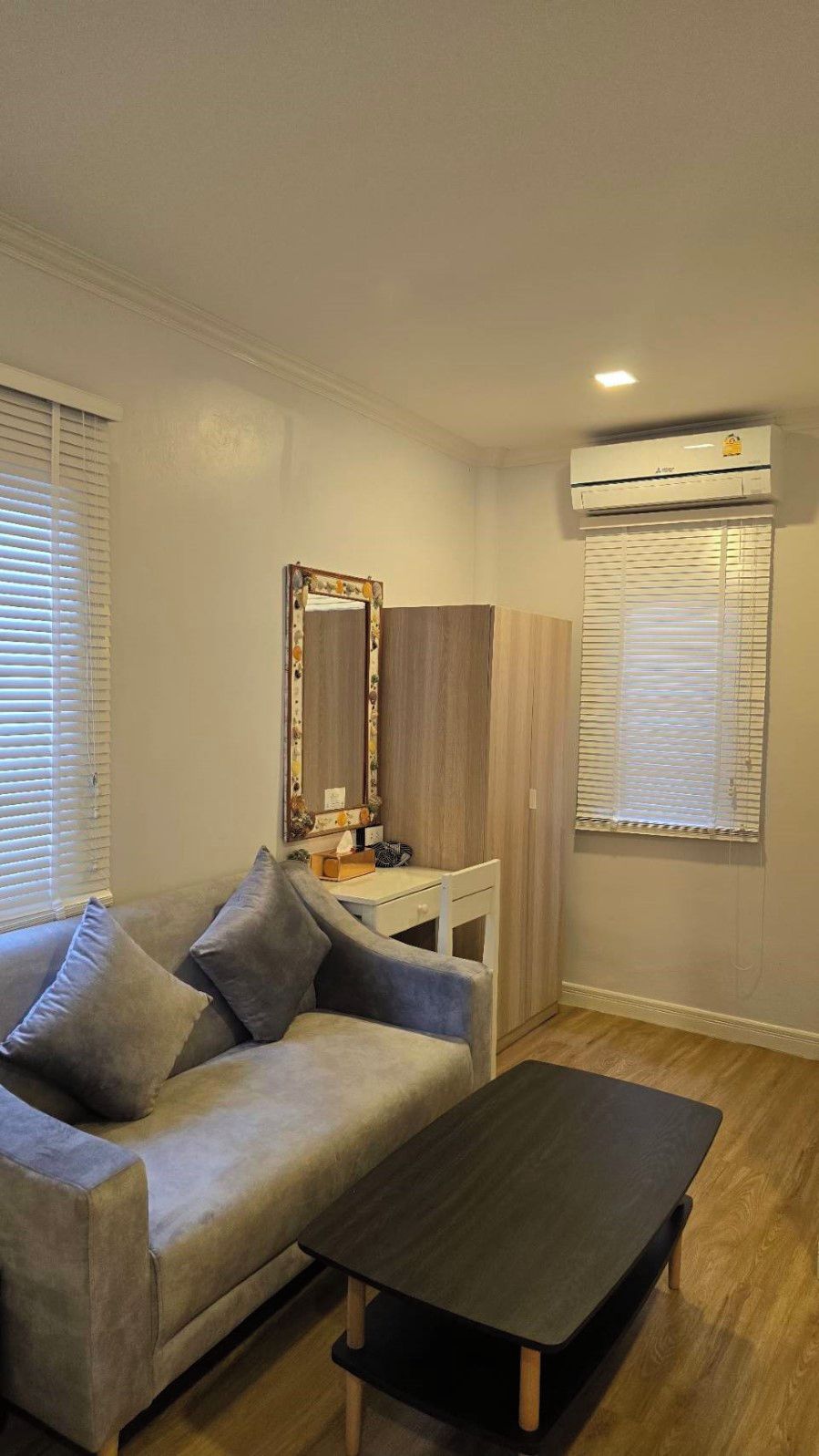 A living room with a sofa, a coffee table, a side table, a mirror, and an air conditioning unit.