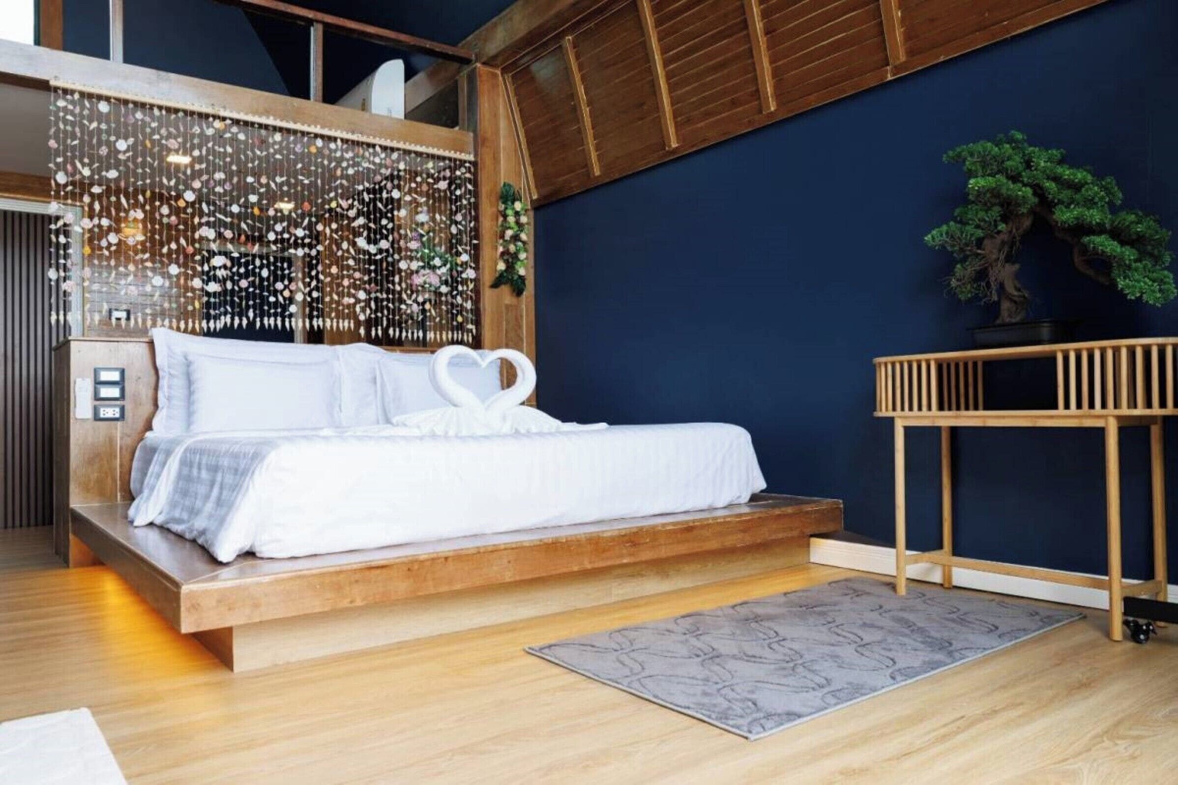 Une chambre à coucher moderne avec un lit surélevé en bois, une décoration murale et un bonsaï.