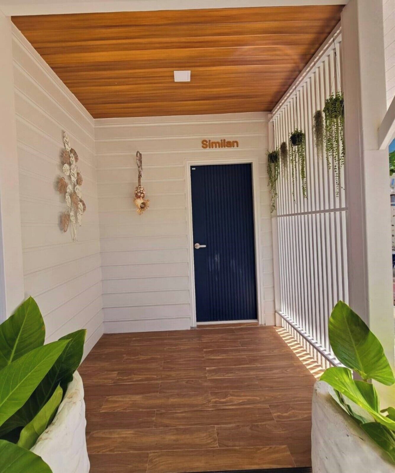 A hallway with a wooden ceiling, a dark blue door labeled "Similan," and potted plants on either side.