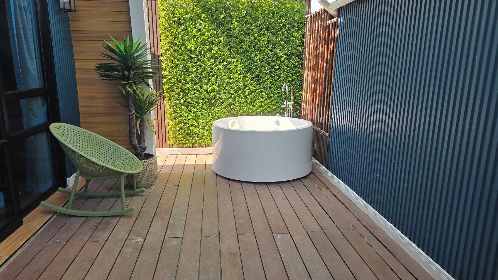 A wooden deck with a green rocking chair and a hot tub.