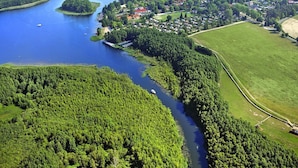 Vista aérea de un pueblo a orillas de un lago, rodeado por un bosque denso que abraza un río.