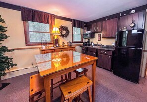 Una cocina con armarios de madera, un refrigerador negro, una mesa de comedor con bancos y una lámpara de pared.