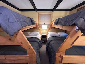 Ein Zimmer mit zwei Etagenbetten, einem kleinen Tisch mit Lampe und einem Fenster mit Jalousien.