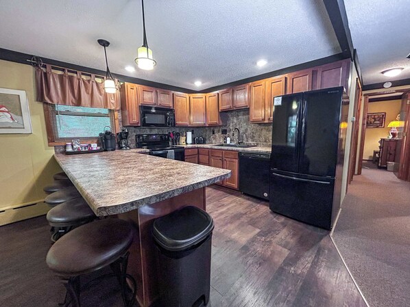 Una cocina con encimeras de granito, armarios de madera, un refrigerador negro y una ventana con persianas.