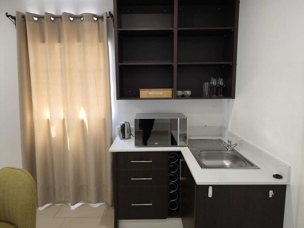 A compact kitchen with a microwave, kettle, and sink.