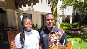 Two people standing in front of a building with a brick pillar and a glass door. There is a tray with drinks and a menu on the ground. - Luxury Loft 2 Levels in Boutique Lodge 2 Ask About our Free Tour (Victoria Falls)