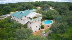 Un edificio de varios pisos con jardín en la azotea, piscina y abundante vegetación circundante.