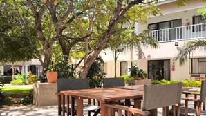 An outdoor seating area with wooden tables and chairs, surrounded by lush greenery and trees. - Room in Lodge - Luxury Suite in Zambezi Boutique Lodge 2, Free 4x4 Town Tour (Victoria Falls)