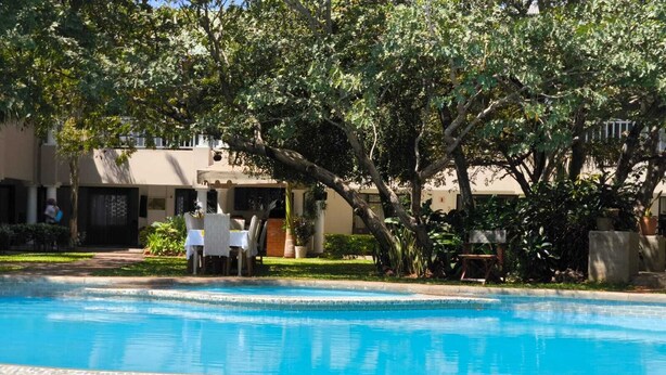 A swimming pool with a tiled edge, surrounded by greenery and a building with a patio area. - Room in Lodge - Luxury Suite in Zambezi Boutique Lodge 2, Free 4x4 Town Tour (Victoria Falls)