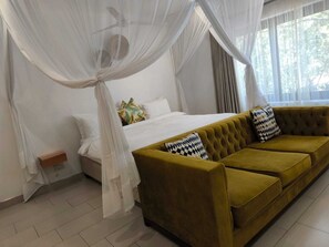 A bedroom with a bed, a sofa, a nightstand, and a window with curtains. - Room in Lodge - Luxury Suite in Zambezi Boutique Lodge 7 Free Tour Availaible (Victoria Falls)