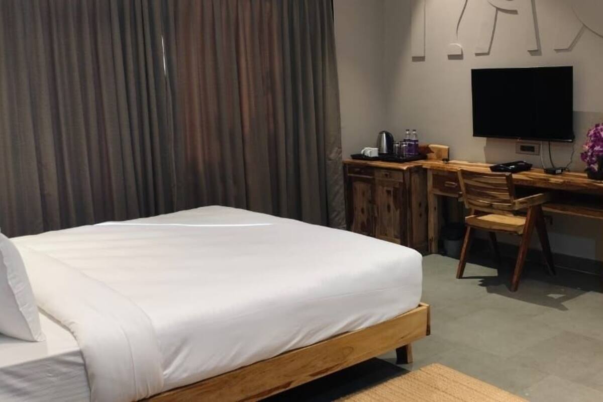 Une chambre à coucher comprenant un lit, un bureau, une chaise, un téléviseur et un banc en bois.