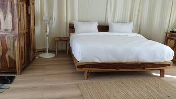 Uma cama de madeira com roupa de cama branca em um quarto com piso de madeira e uma janela grande com cortinas.