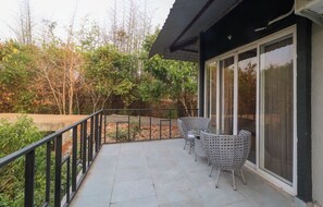 Ein Balkon mit Glastür, Gartenmöbeln und Blick auf Bäume und eine Brücke.