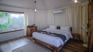 A bedroom with a wooden bed, a bedside table with a lamp, a window with curtains, and an air conditioning unit. - Shiv Ganga Kanha Resort (Baihar)