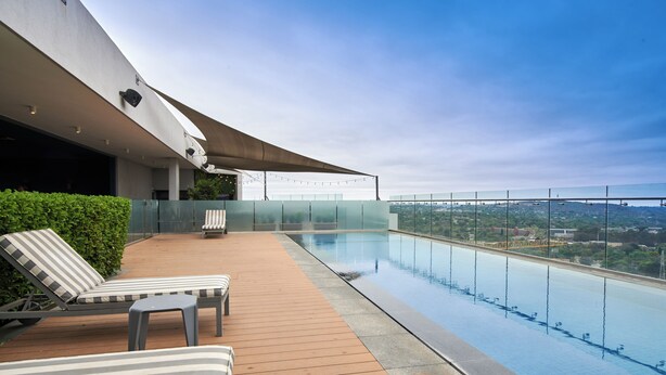 A rooftop infinity pool with lounge chairs and a wooden deck.
